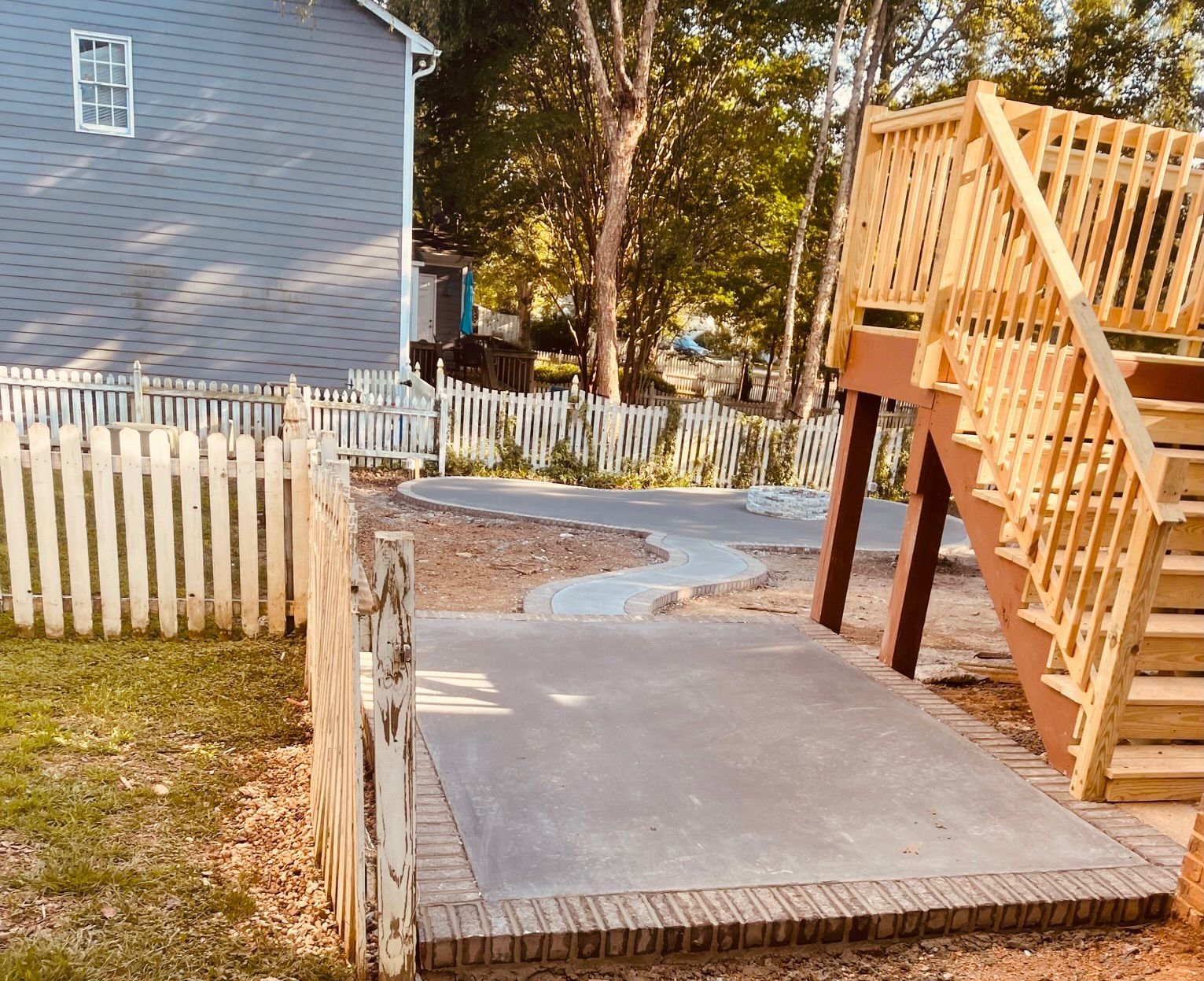 Backyard with wooden play structure, concrete paths, picket fences, and a gray house.