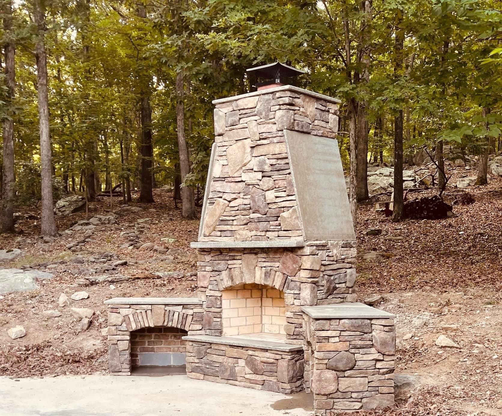 Stone outdoor fireplace in wooded area.