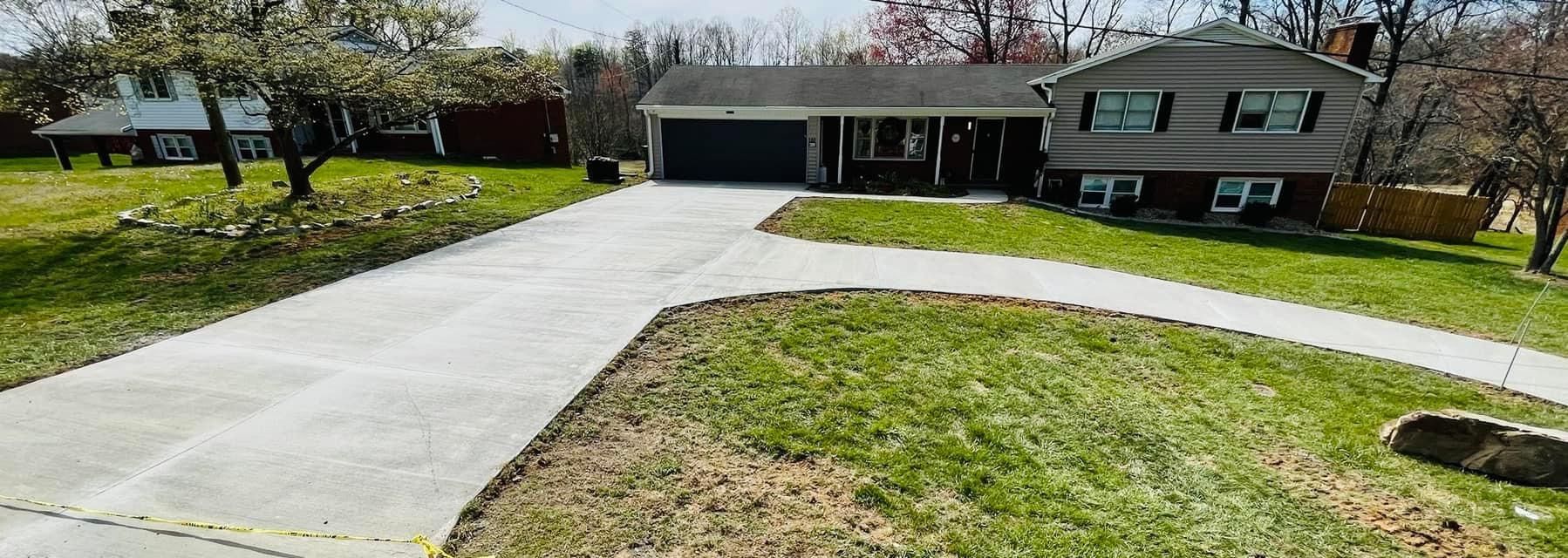 House with driveway and green lawn. Gray roof, black garage door. Trees in background.