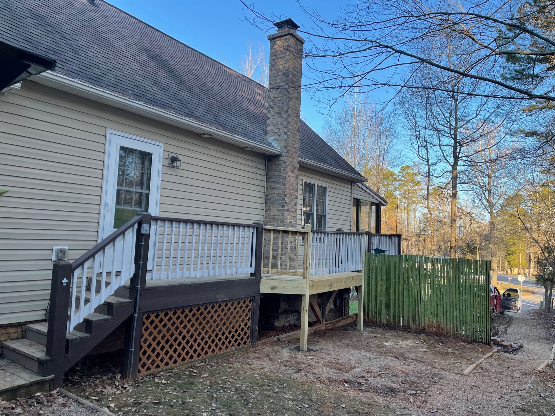 Side view of a house with a deck, a chimney, and a partially visible fence.