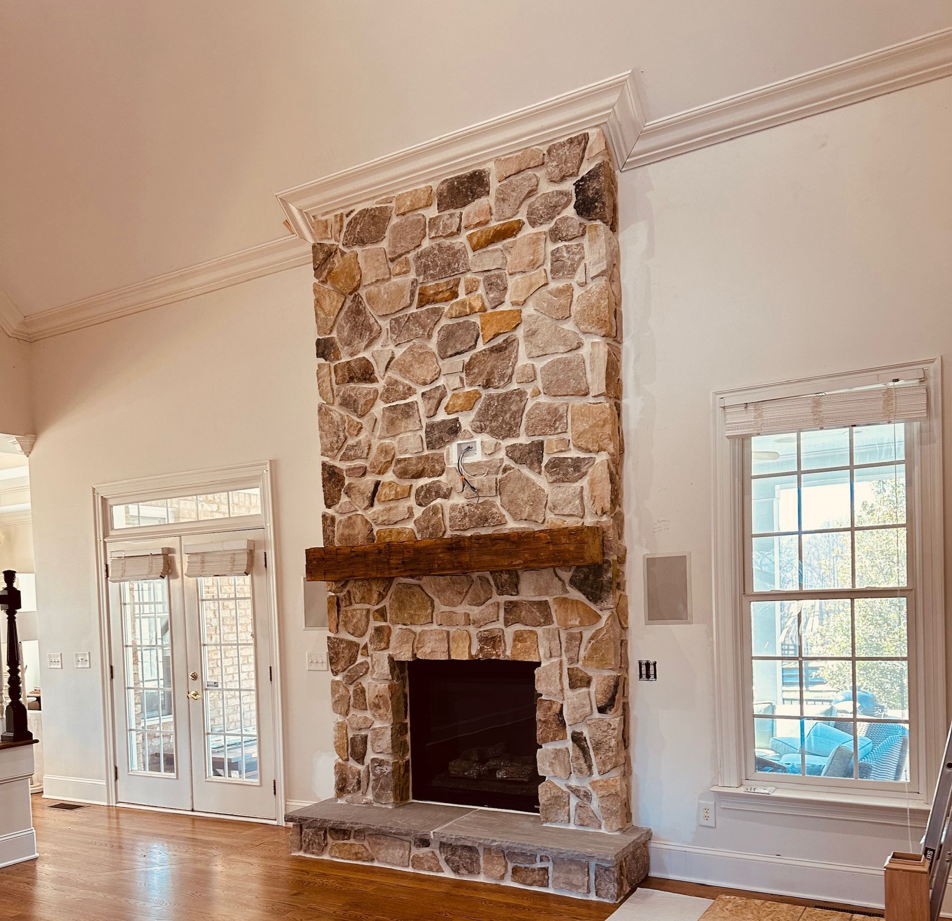 Stone fireplace with a wooden mantel in a white-walled room with wooden floors and windows.