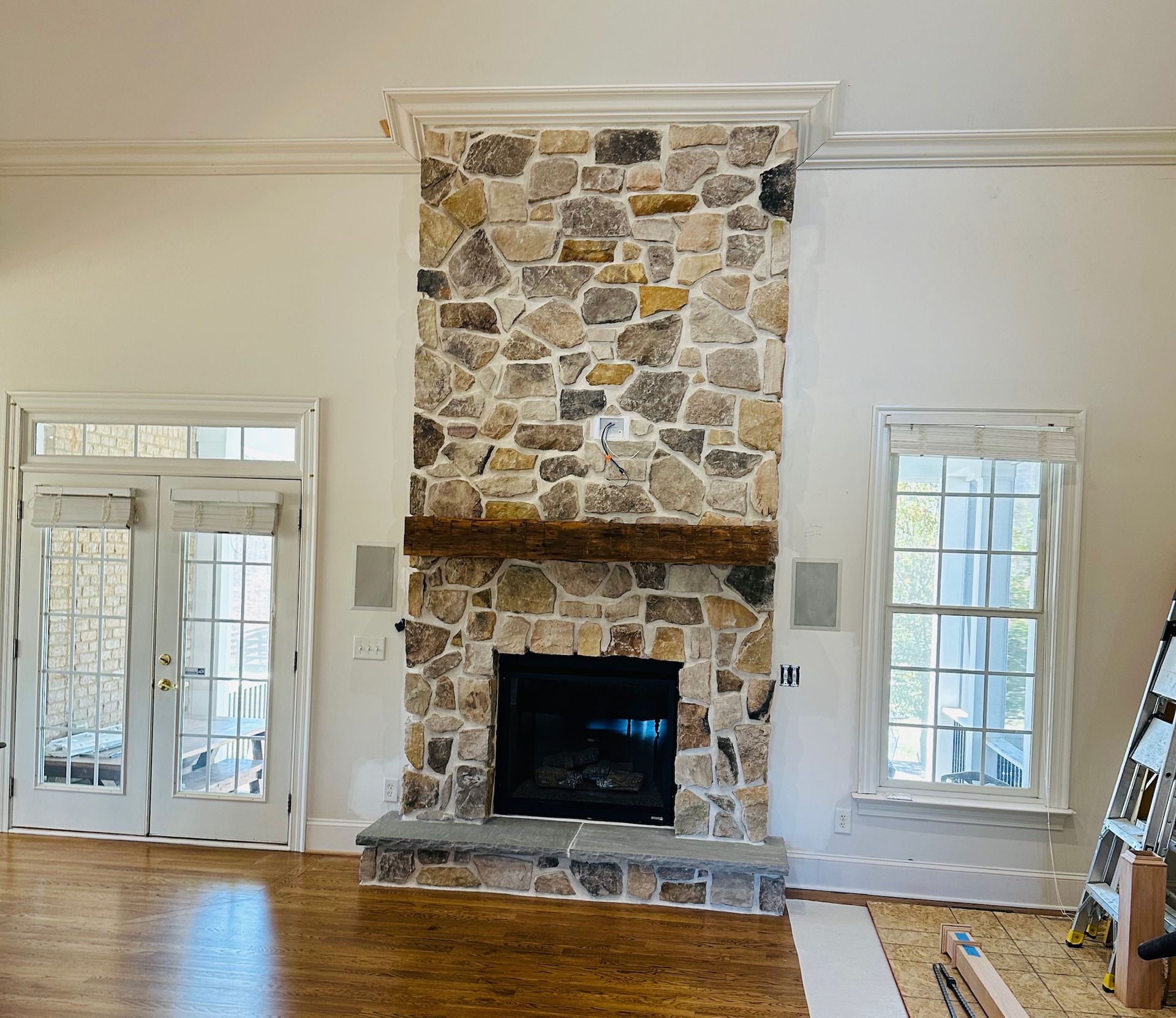 Stone fireplace with wooden mantle, flanked by white doors and a window in a living room.