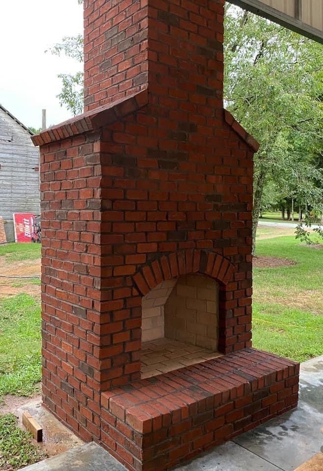 Brick outdoor fireplace with arched opening and chimney.