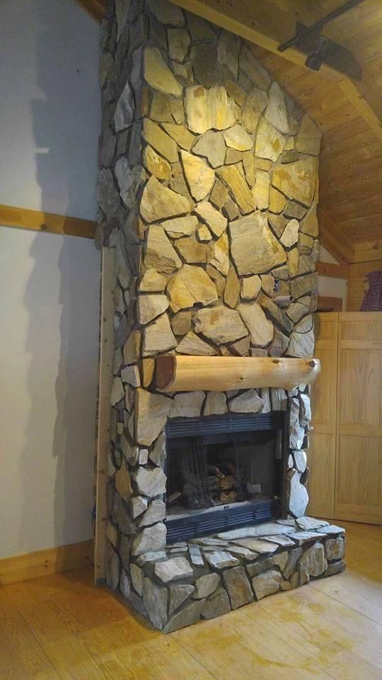 Stone fireplace in a room with wooden floors, light-colored stone, and a wooden beam mantel.
