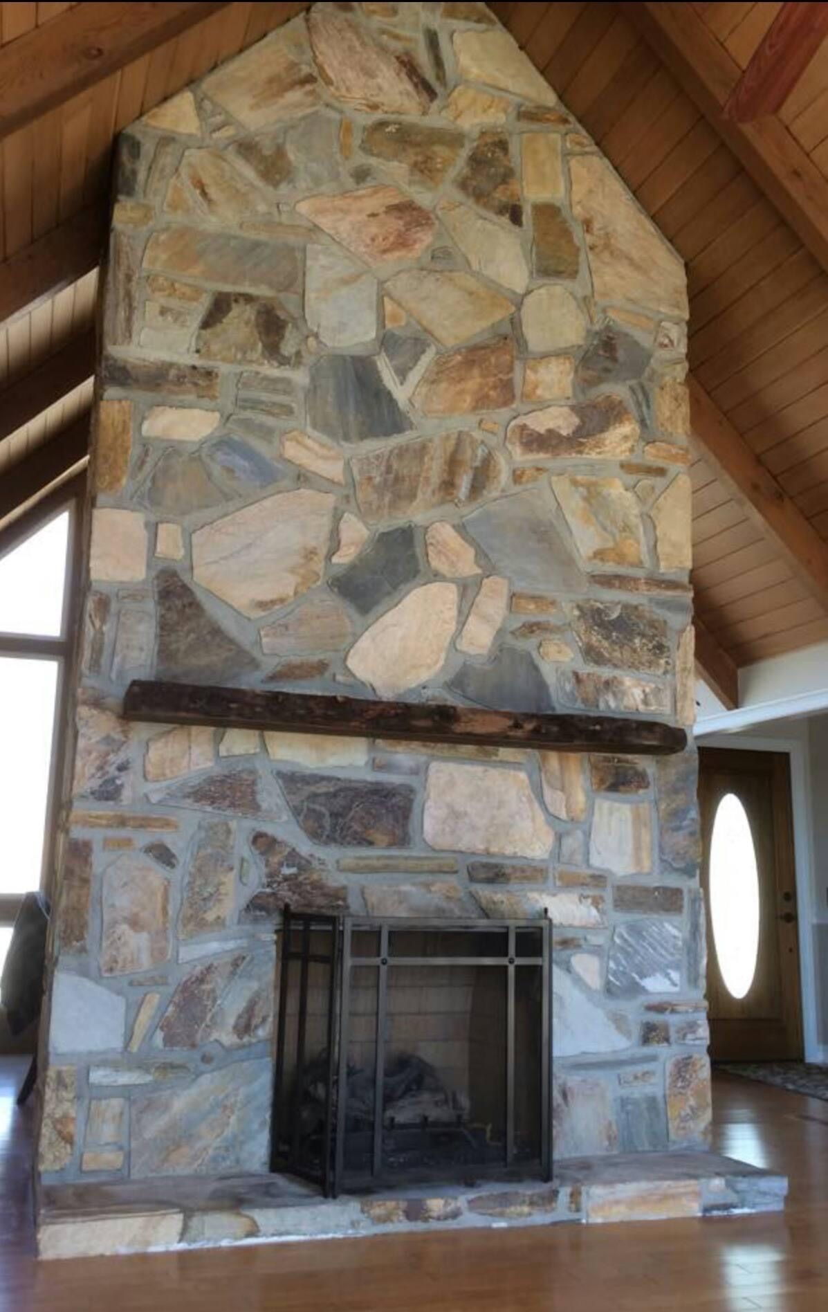 Stone fireplace with dark screen and wooden beam, inside a room with wooden floor and door.