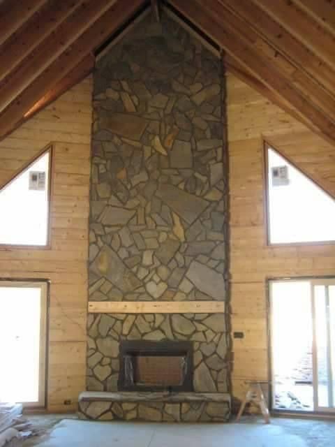 Stone fireplace in a wooden-paneled room with triangular windows and vaulted ceiling.