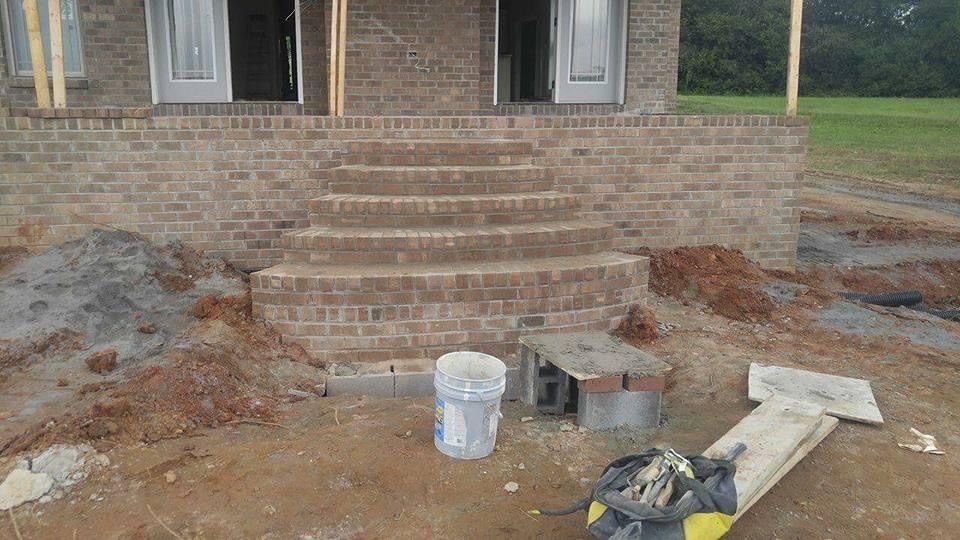 Brick steps leading to a house under construction. Earth and construction debris surround the stairs.