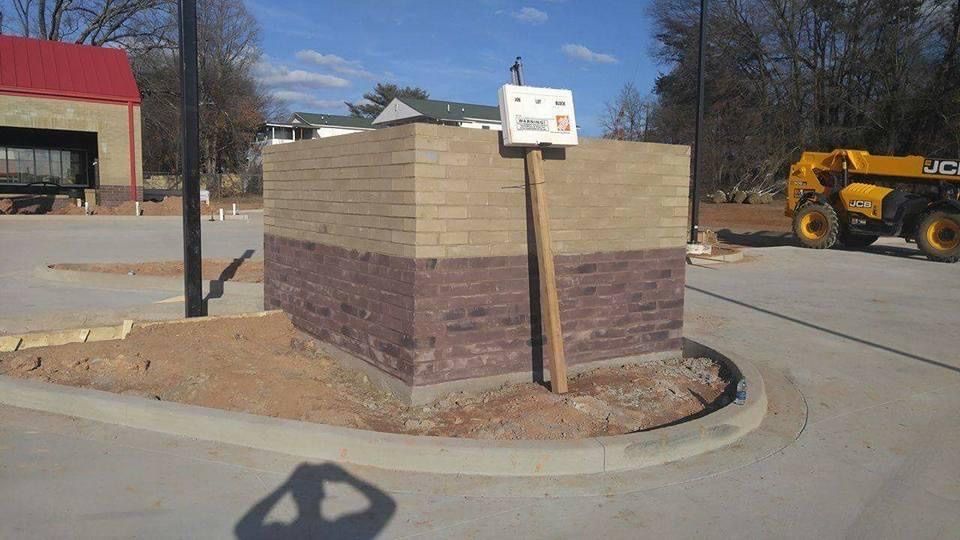 Brick and concrete structure with sign in parking area; construction equipment visible.