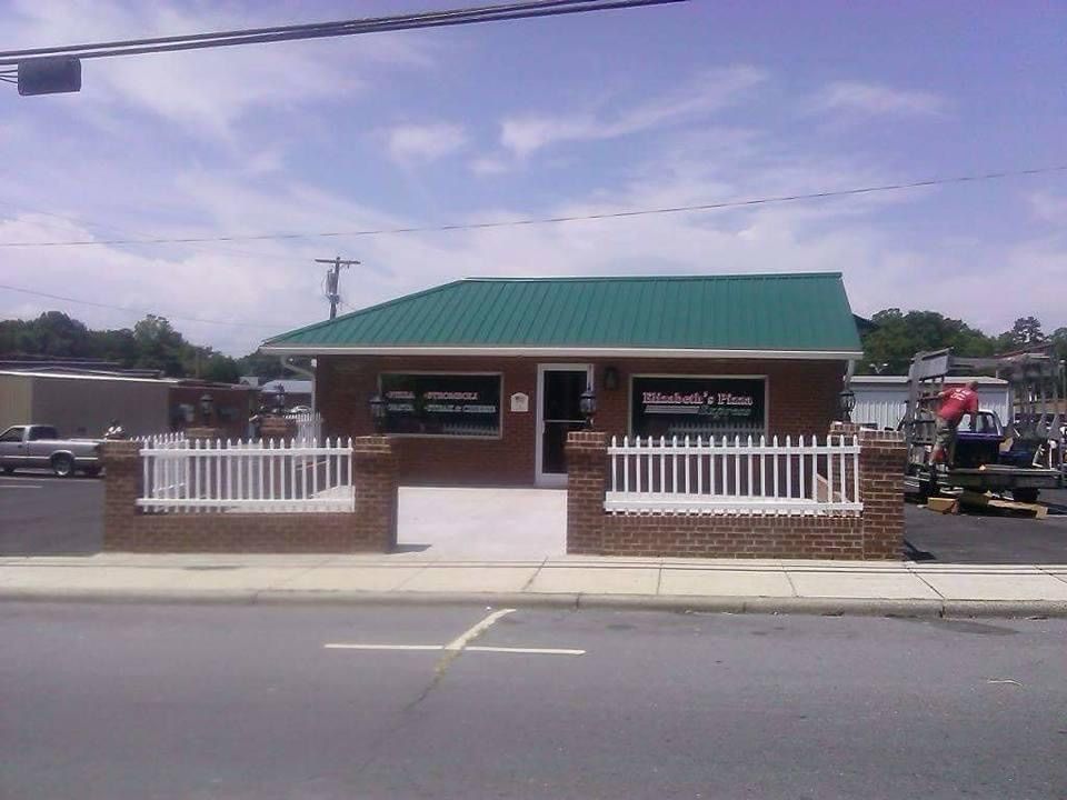 Elizabeth's Pizza storefront. Red brick building with a green roof and white picket fence in front.
