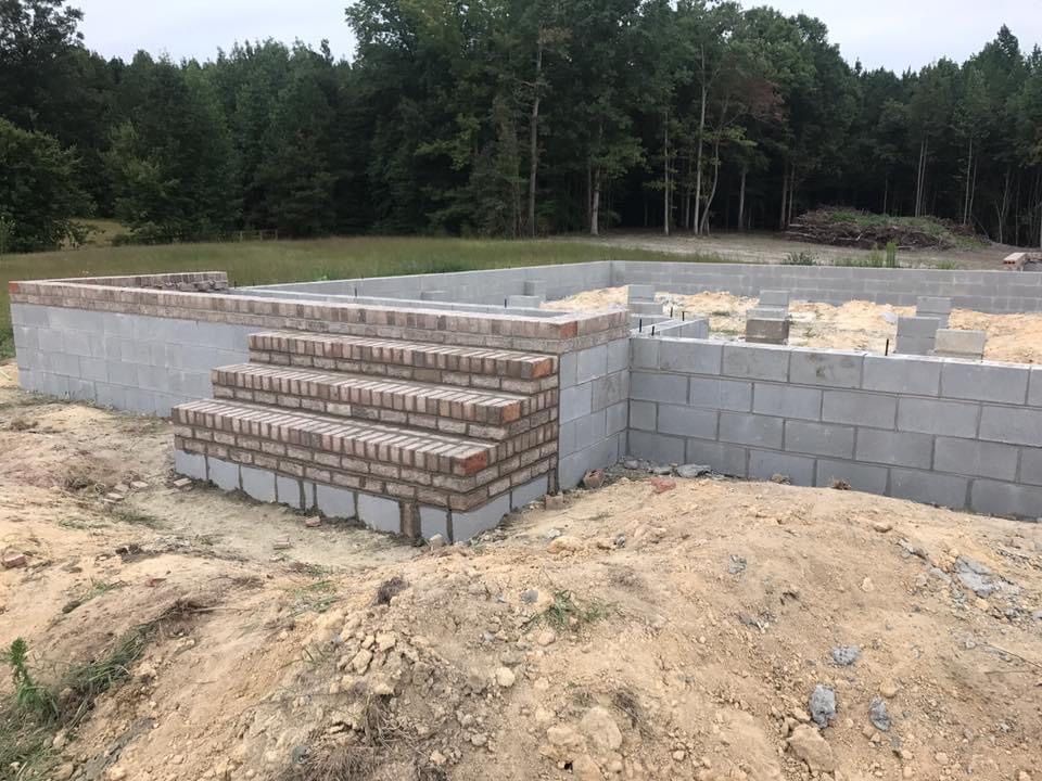 Foundation of a building under construction, with brick steps and cinder block walls, outdoors.