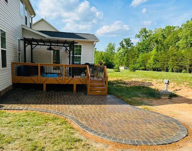 Wooden deck with pergola, brick patio, and house in backyard on a sunny day.