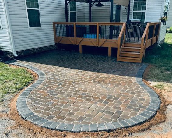 Brick patio with curved edge next to a wooden deck, next to a white house.