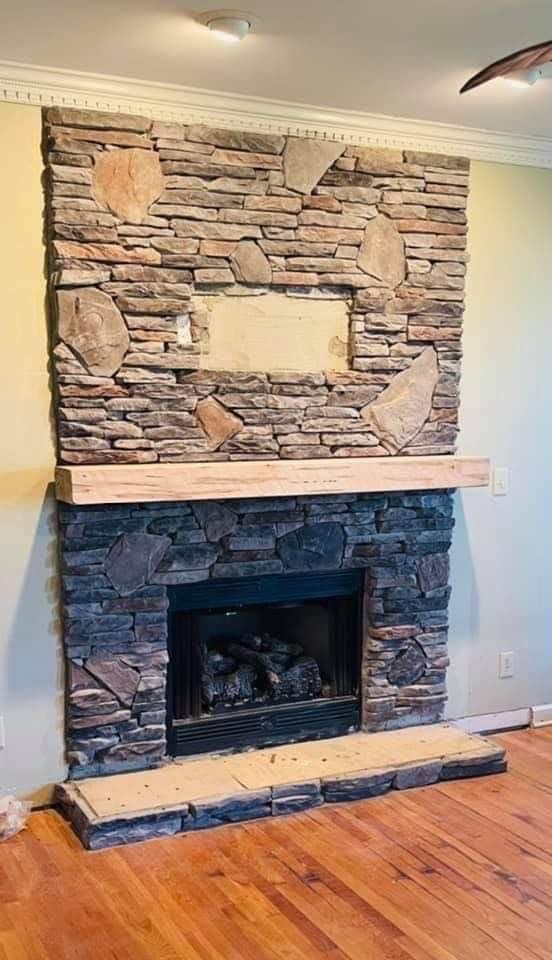 Stone fireplace with wooden mantle and hearth, in a room with hardwood floors and off-white walls.