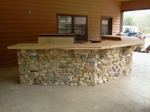Stone outdoor bar with tan countertop, under a wooden awning.