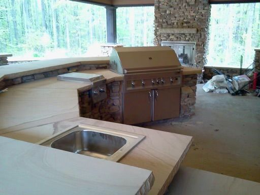 Outdoor kitchen with stainless steel grill, stone counter, and sink.