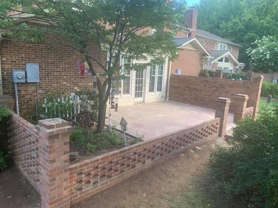 Brick patio with decorative walls near a brick house and garden.