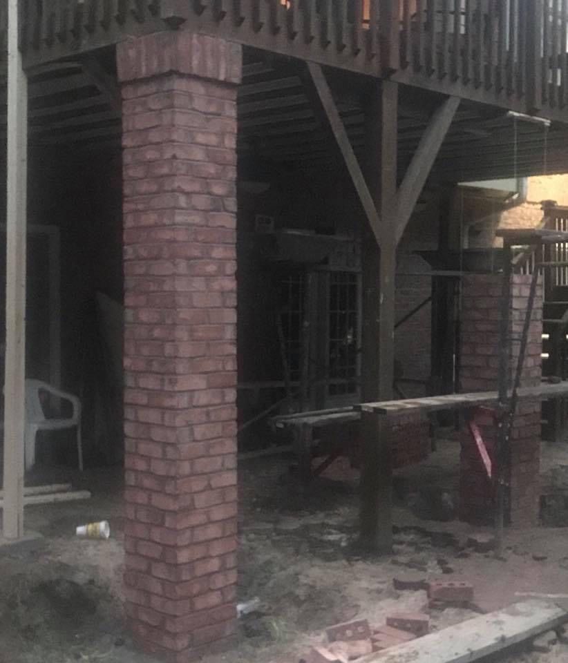 Brick pillars supporting a wooden deck. Construction materials scattered below.