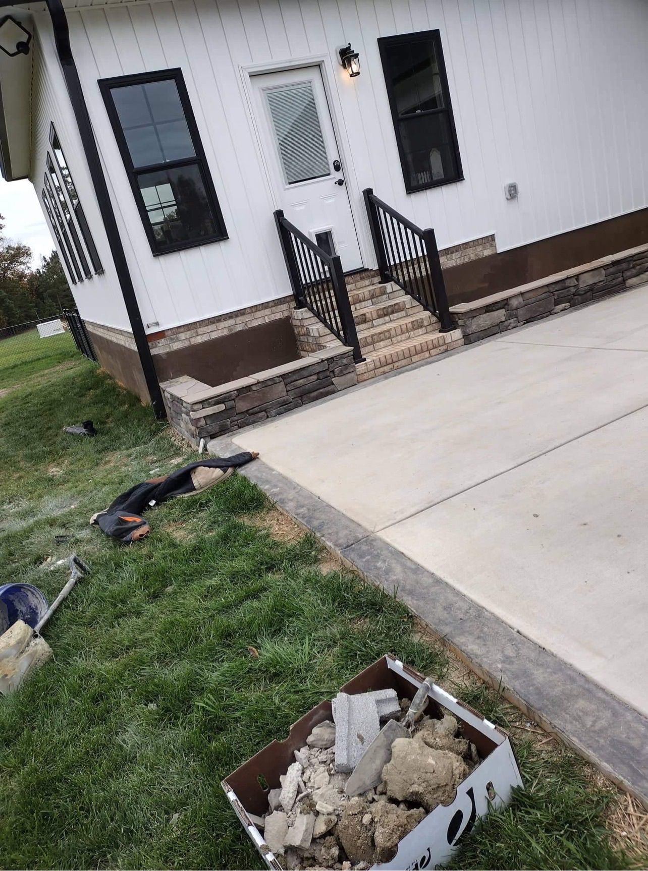 Exterior of a modern white house with black trim, concrete driveway, and a stone facade on the foundation.