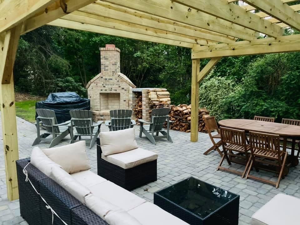Outdoor patio with pergola, seating areas, a fireplace, and woodpile.