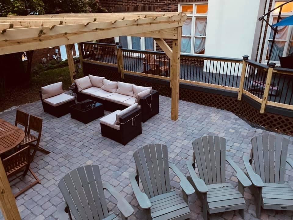 Outdoor patio with seating: L-shaped sofa under pergola, Adirondack chairs, stone pavers, and wooden deck.