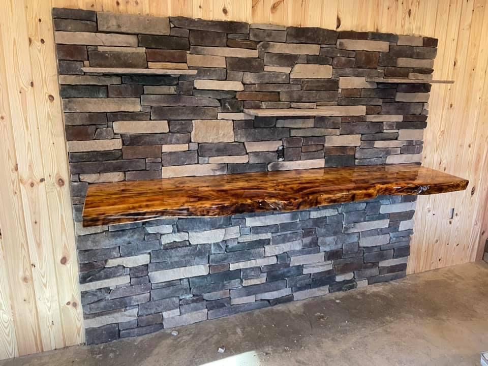Stone-covered wall with a live-edge wood bar, shelving. Rustic interior, neutral tones.