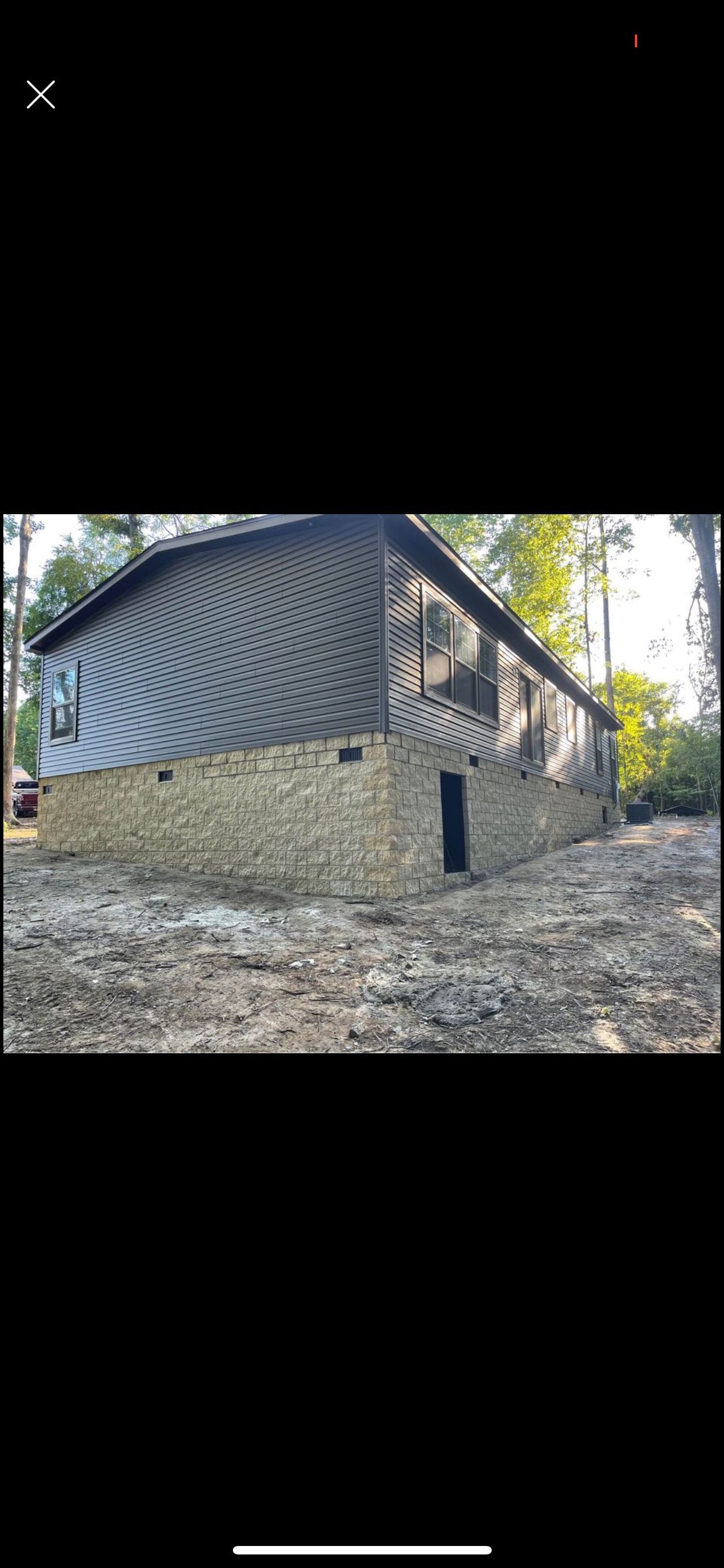 A two-story house with dark siding, set in a wooded area. The bottom level is stone.
