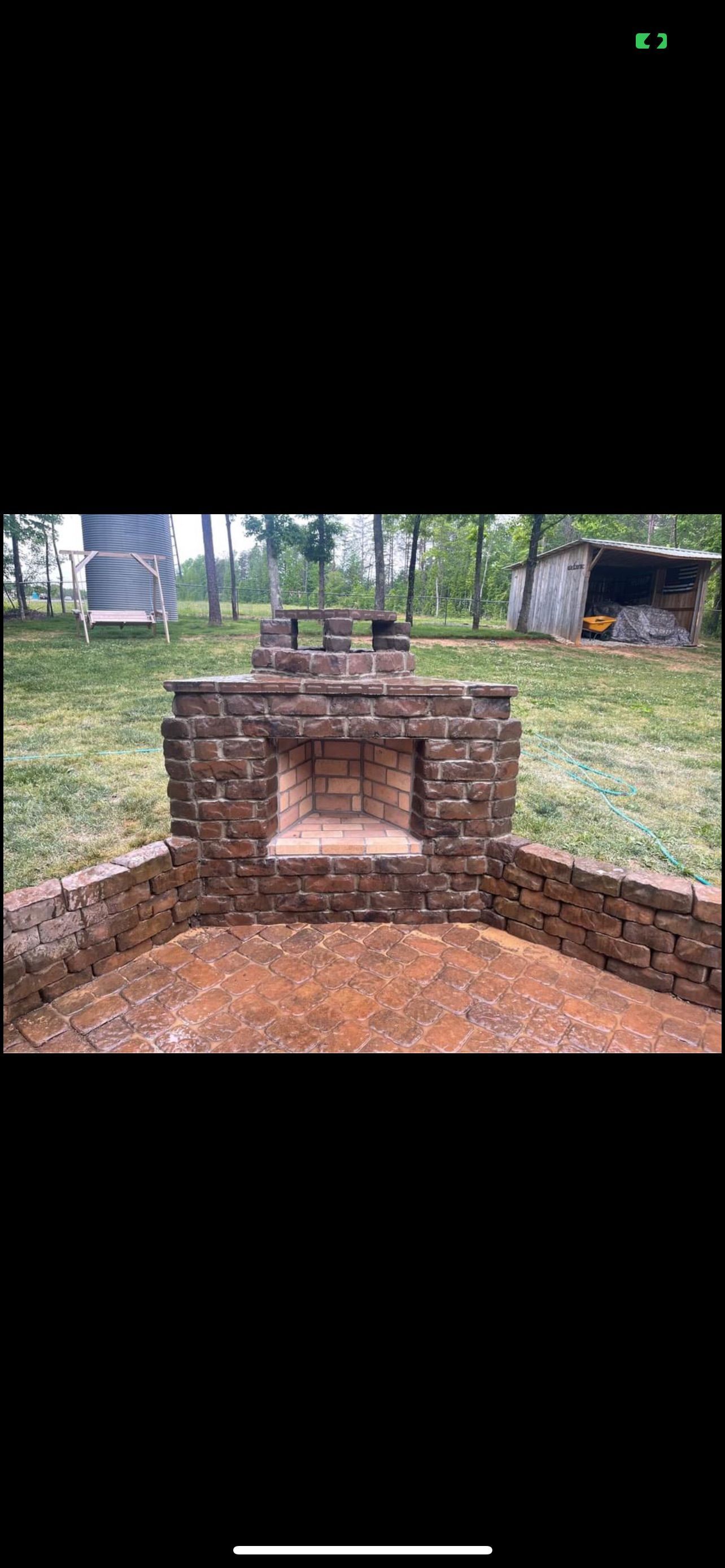 Brick structure with a recess, in a grassy area. Trees and a shed are in the background.