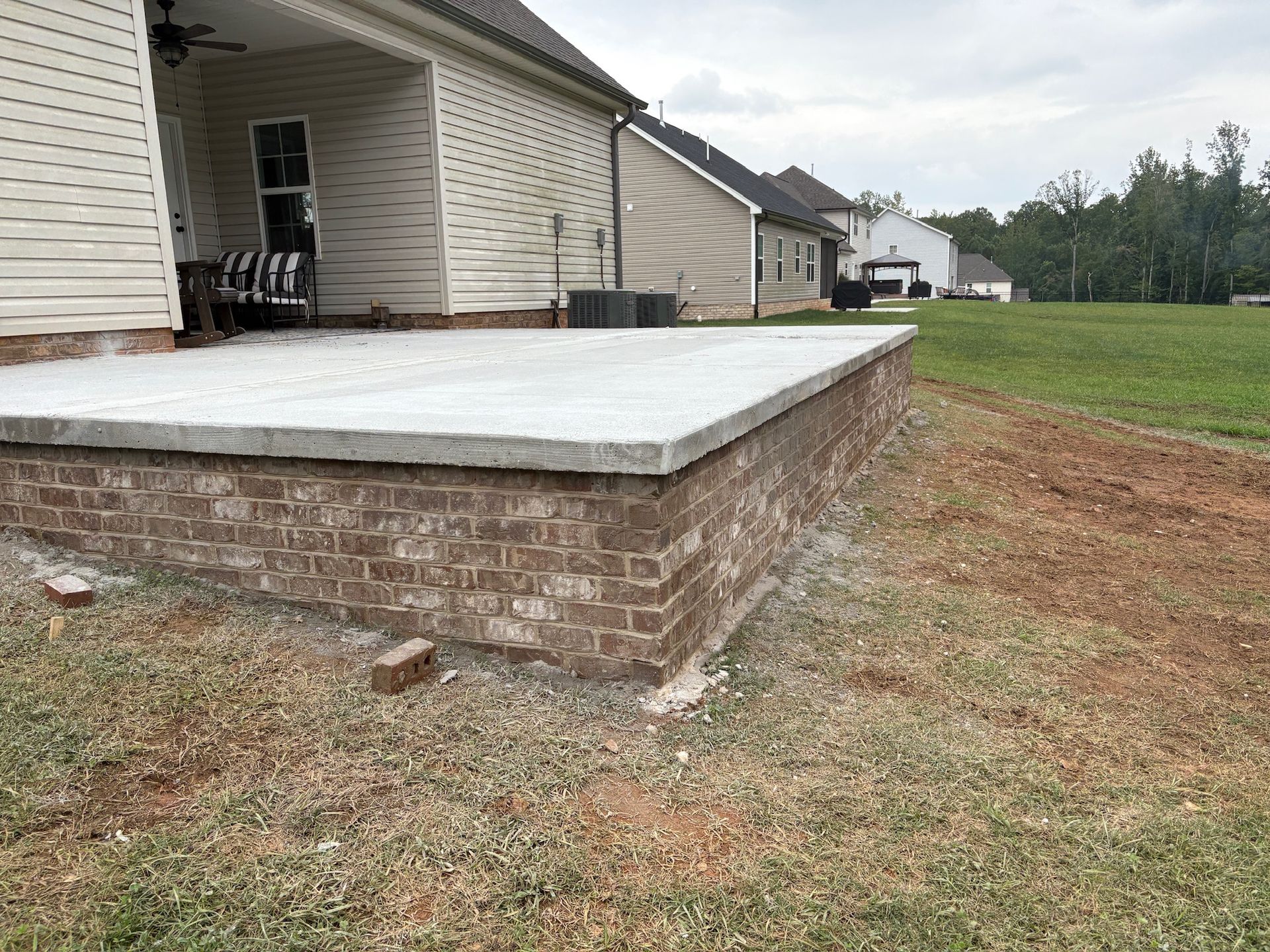 Brick patio with concrete top, next to house and grassy yard.
