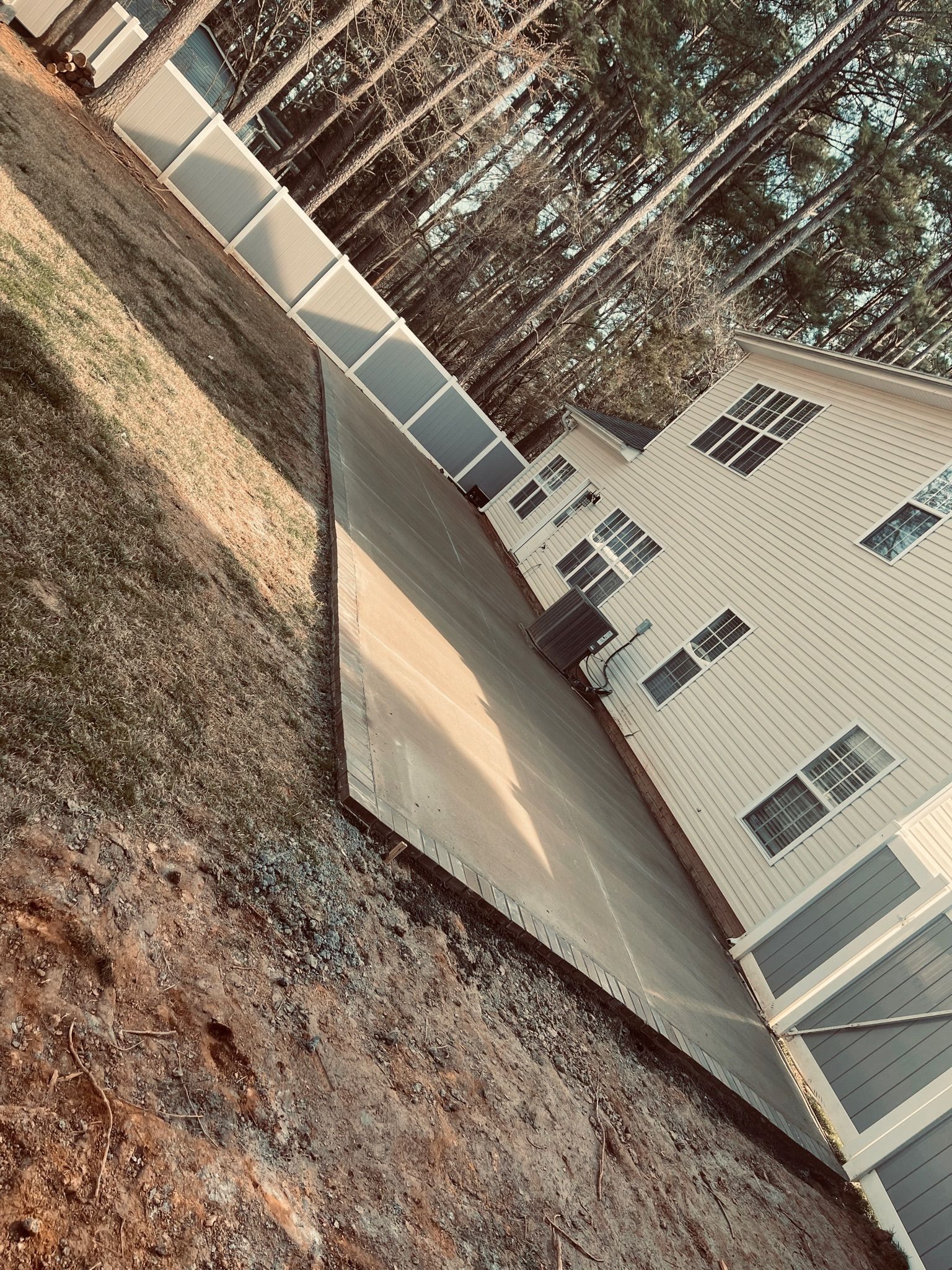 Sideways view of a beige house with a driveway and walkway on a hill, trees in the background.