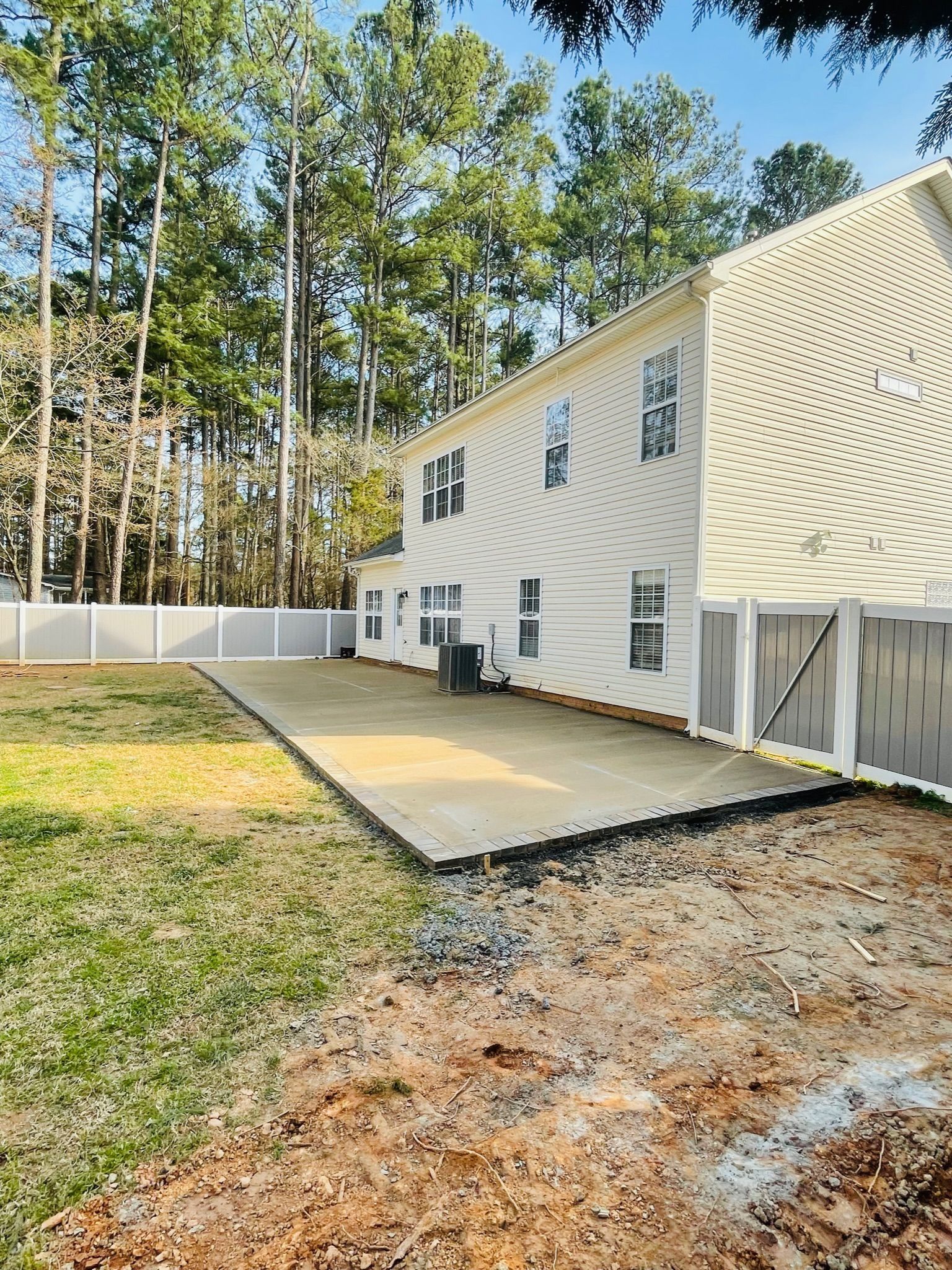 Backyard with a newly built patio next to a white house. Green grass, trees, and a white fence.