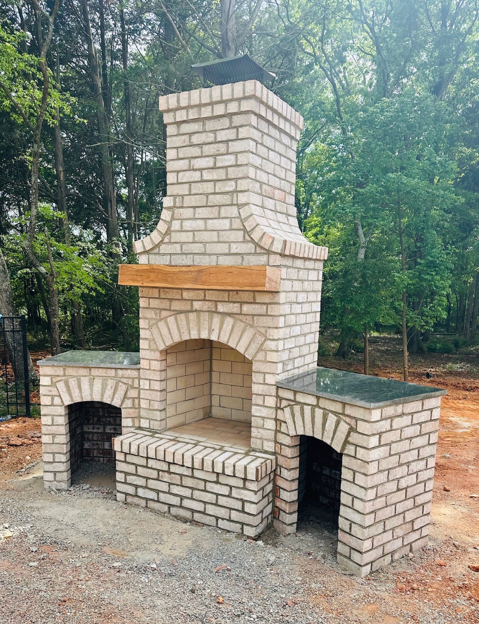 Brick outdoor fireplace with arched openings and wooden mantel.
