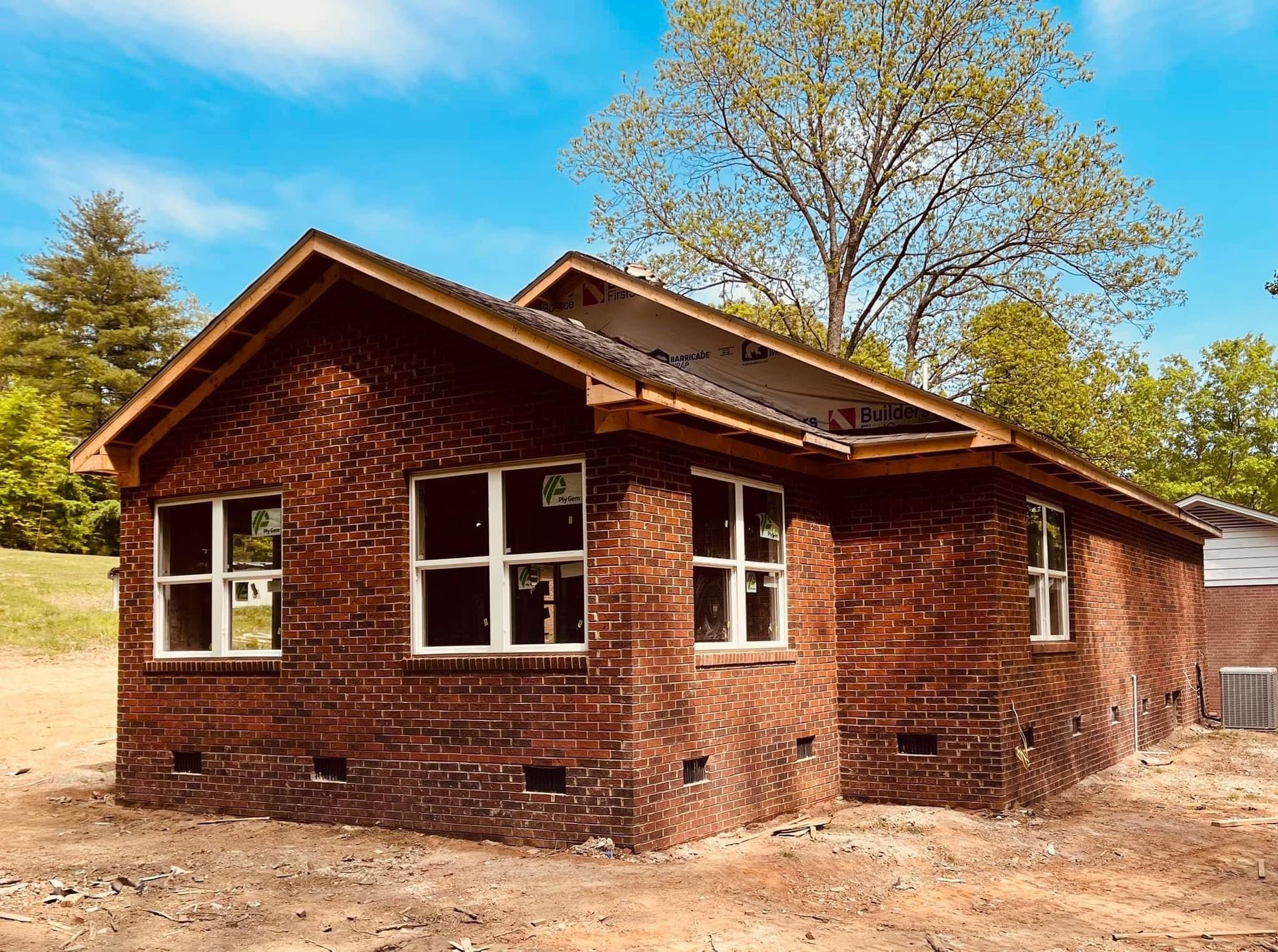 Brick house under construction with white-framed windows. Roof framework visible.
