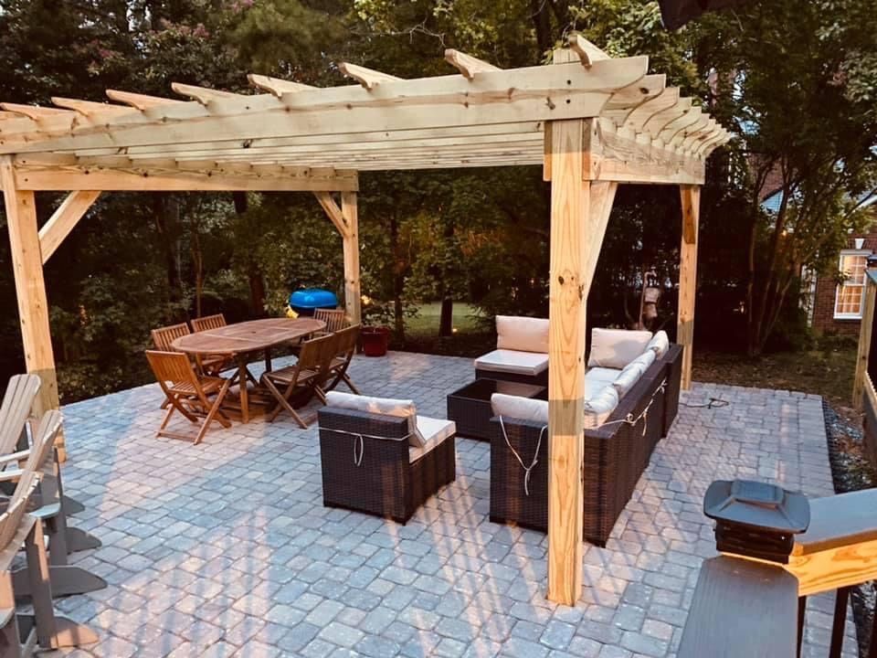 Patio with pergola, furniture, and dining table on a brick paved surface.