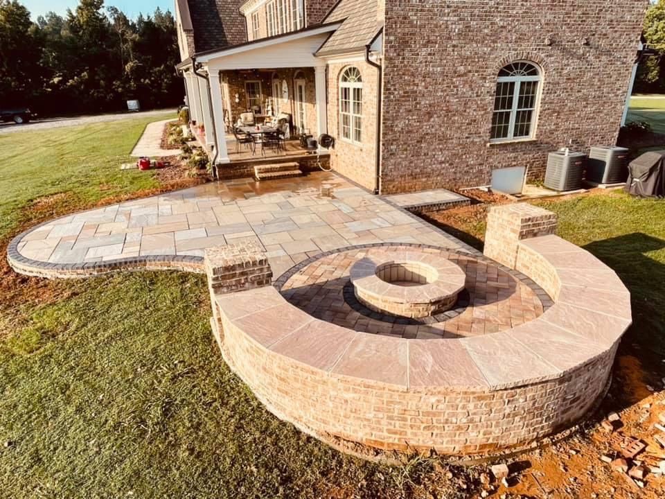 Brick patio with fire pit, lawn, and house with porch in the background.