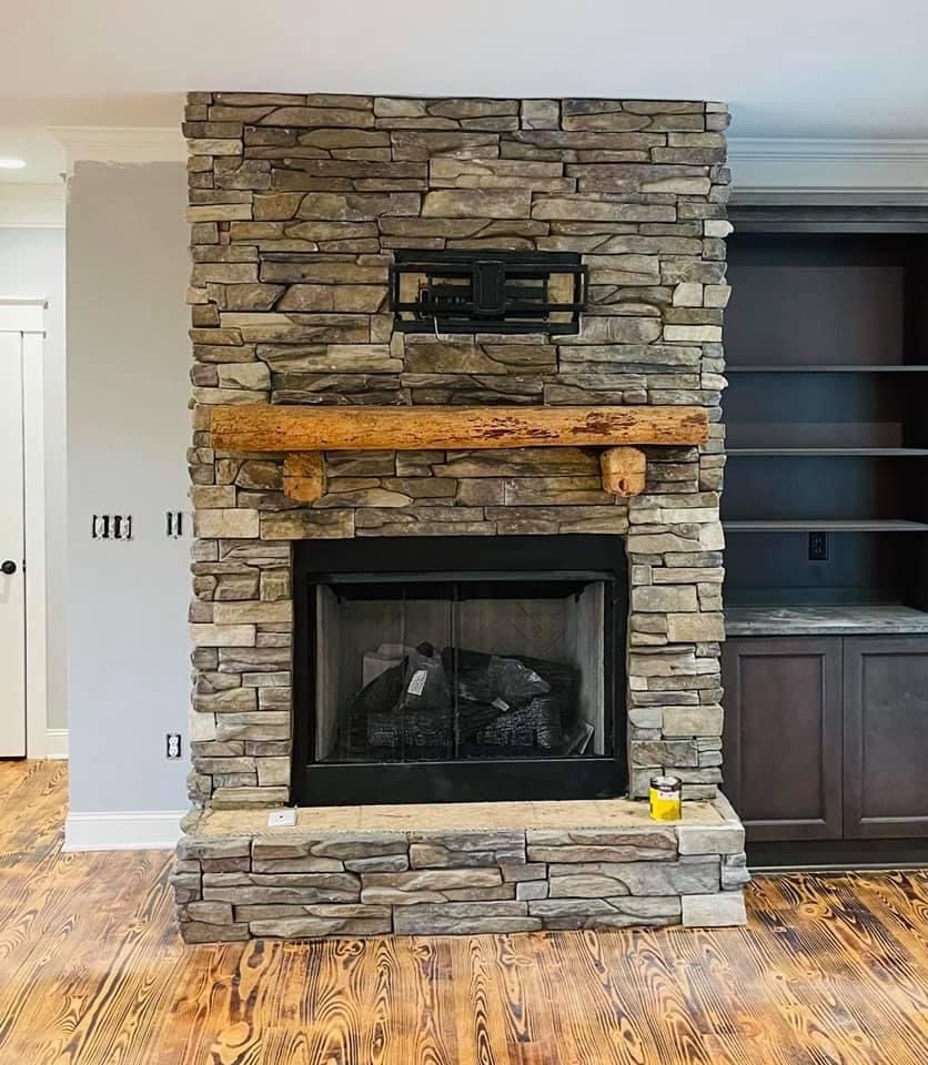 Stone fireplace with wooden beam mantel, black firebox, and built-in shelving.