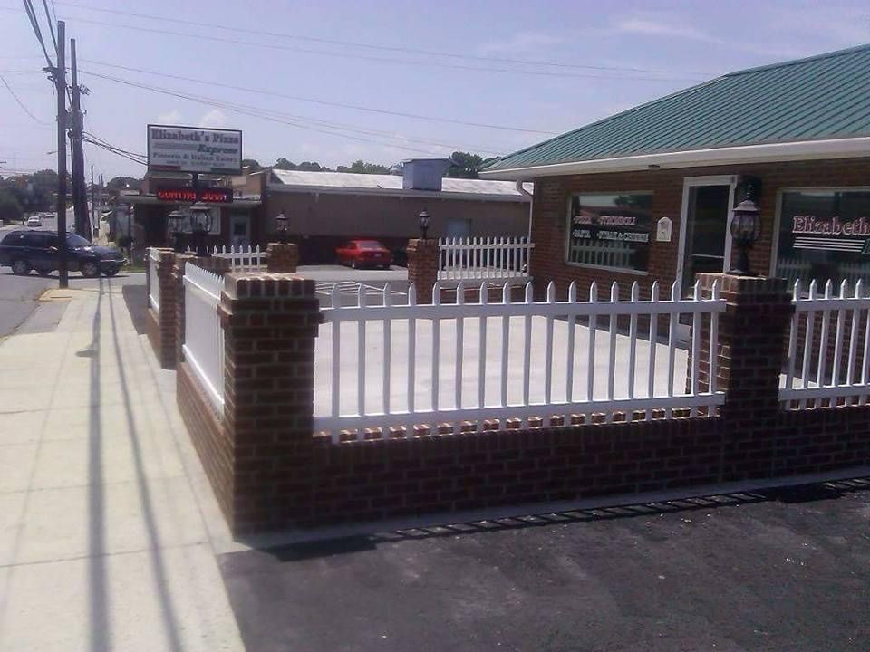 Brick and white picket fence around a small business. The building has a green roof.