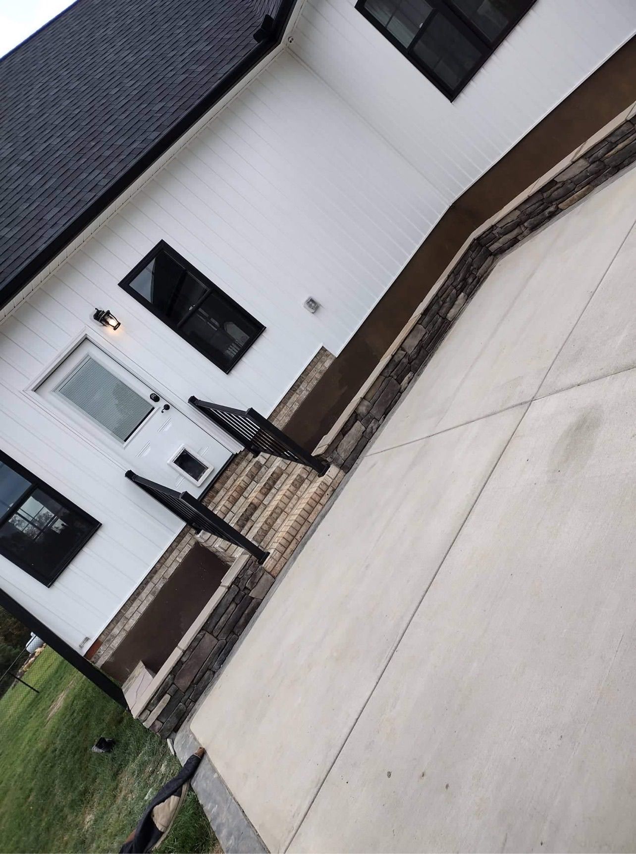 White house with black windows, brown trim, concrete driveway, and black railings.
