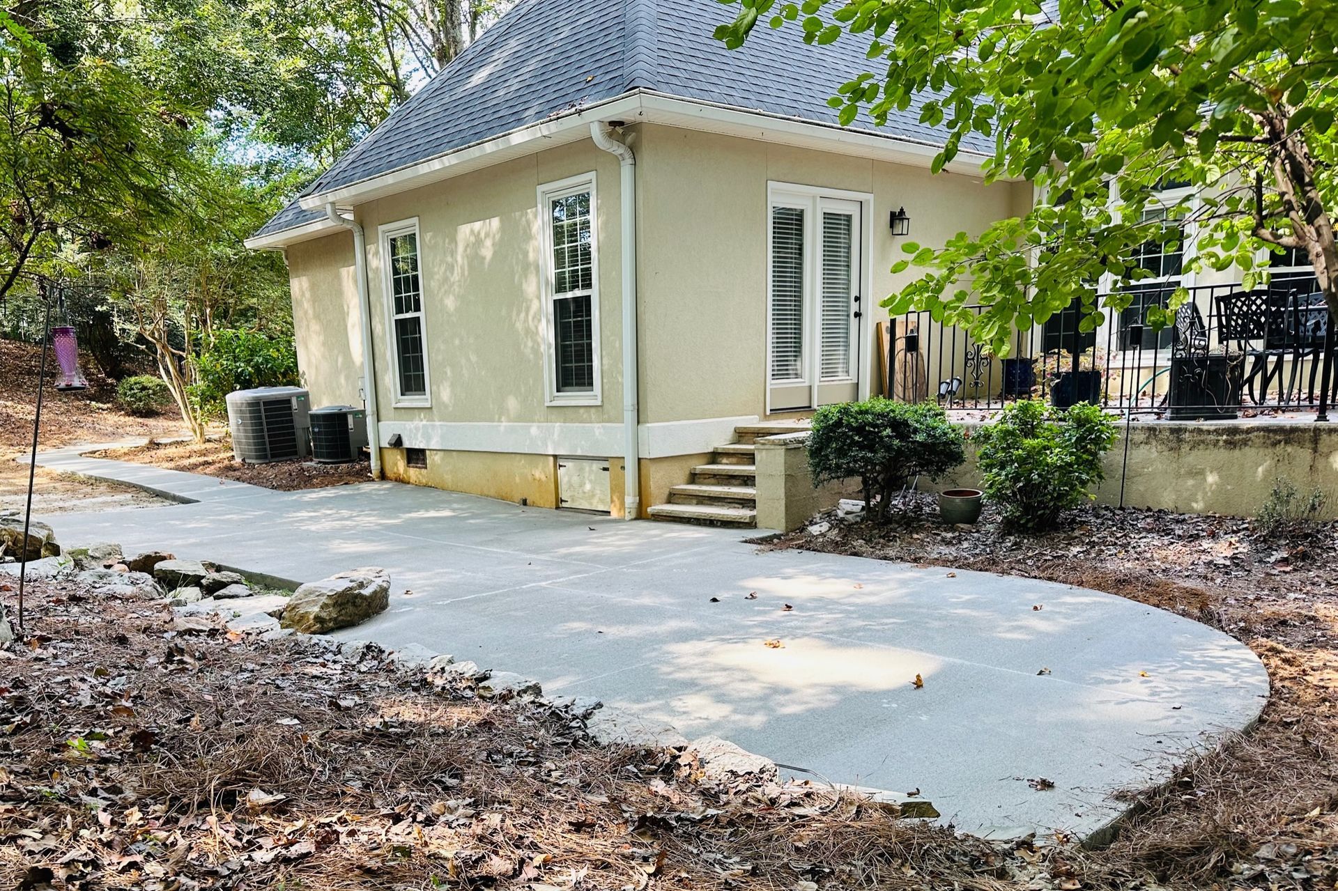 A concrete patio next to a light-colored building with a gray roof, steps, and outdoor furniture.