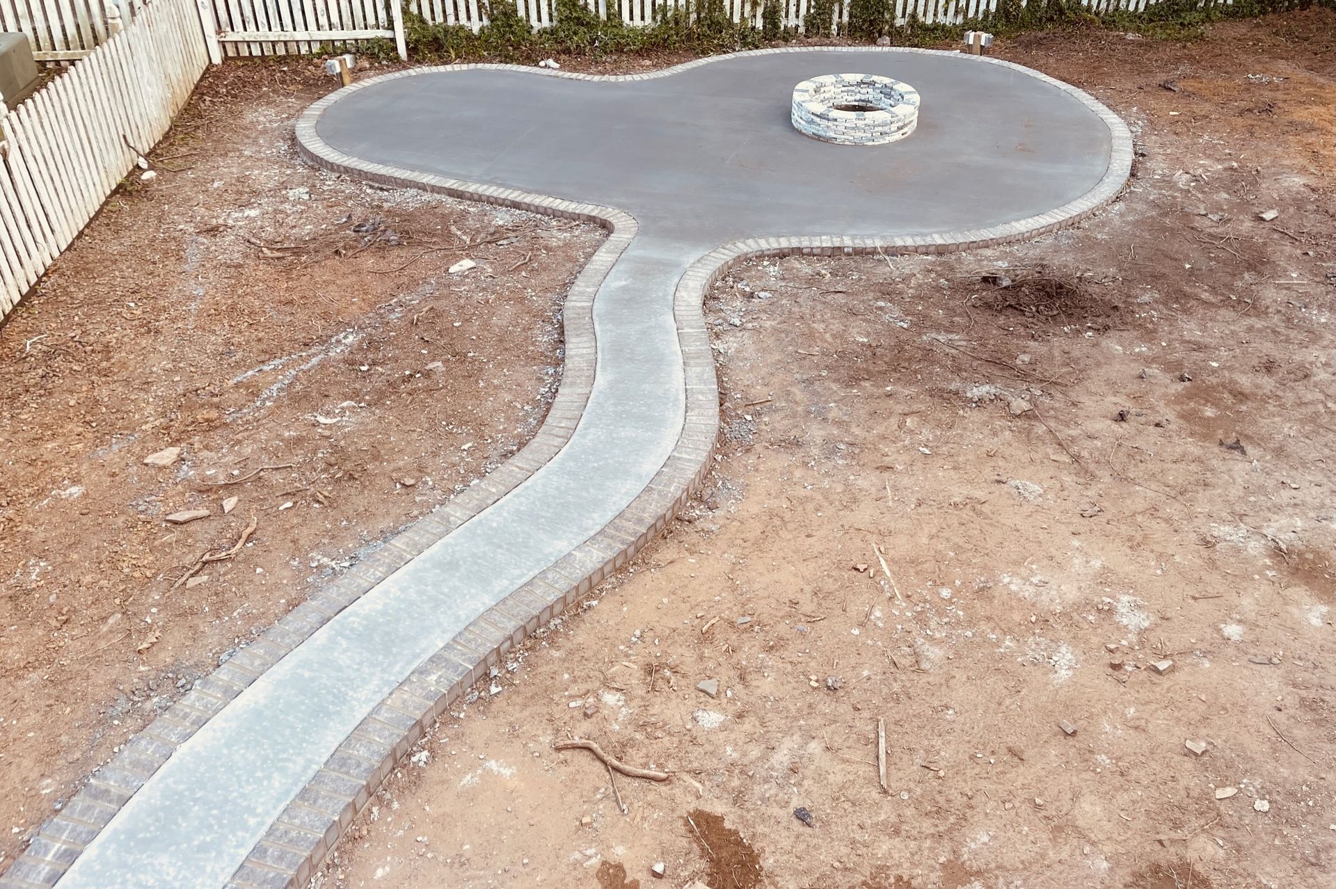A gray concrete patio with a fire pit and a pathway in a yard.