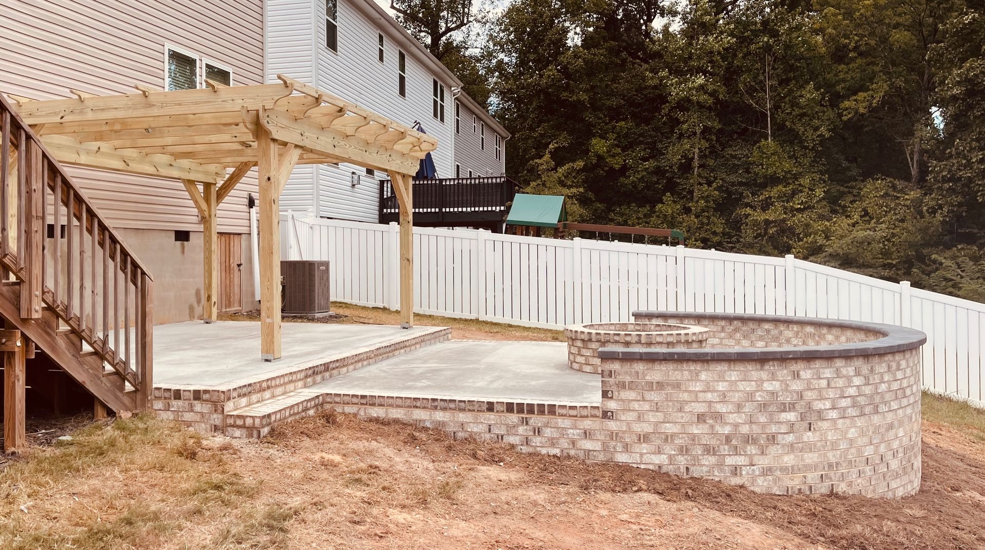 Backyard patio with pergola, brick retaining wall, concrete, and wooden deck.