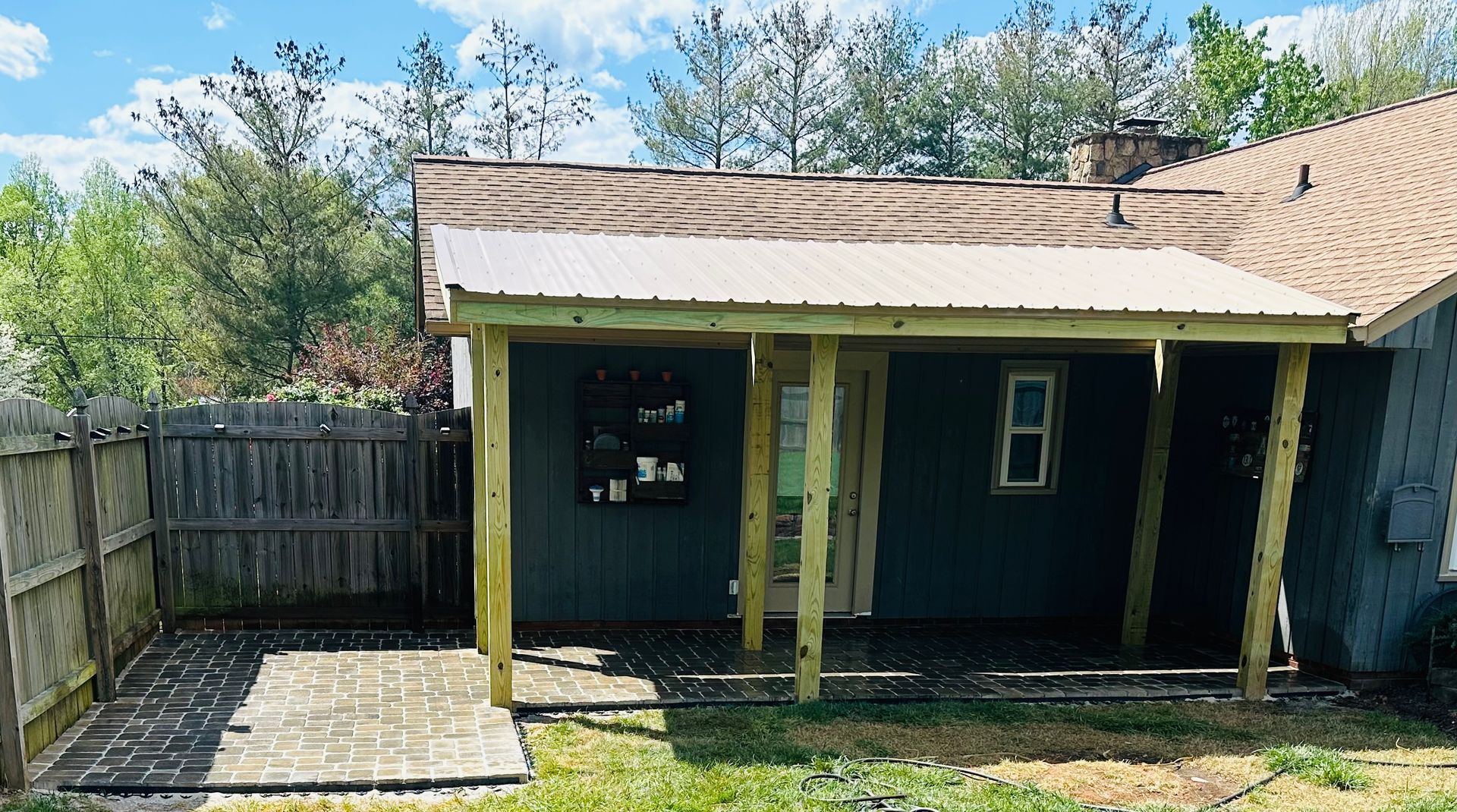 A small teal house with a metal-roofed porch addition and a brick patio.