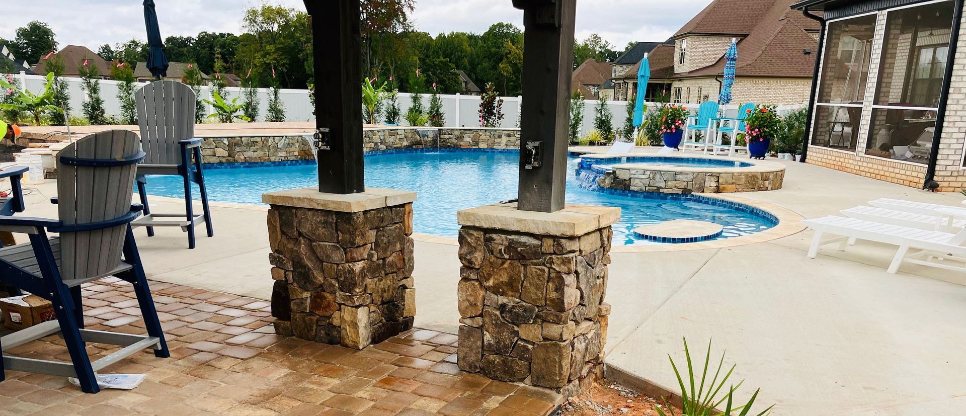 Poolside scene: a pool with a jacuzzi, chairs, and stone pillars.