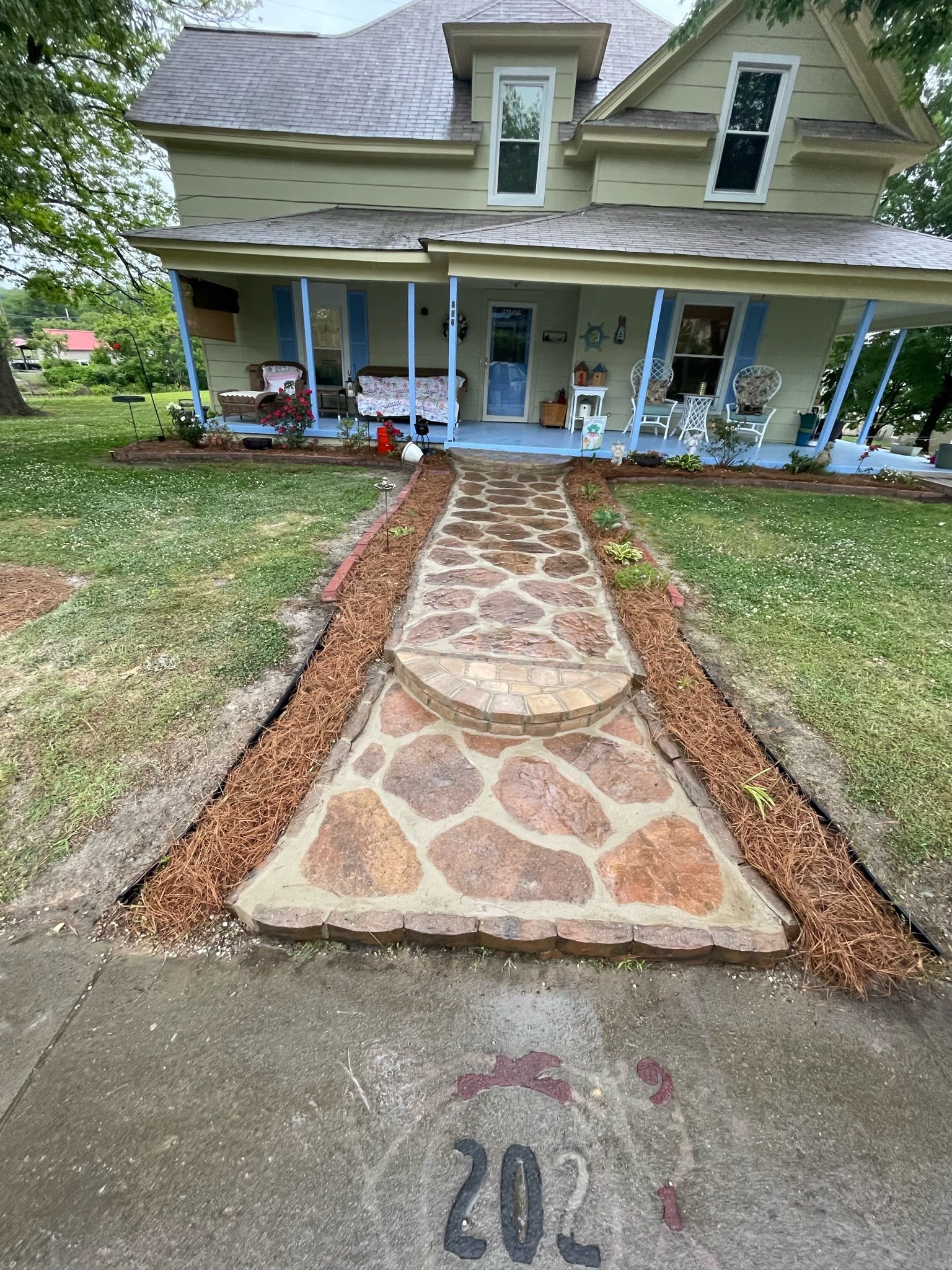 Stone path leading to a light green two-story house with a porch and blue trim.