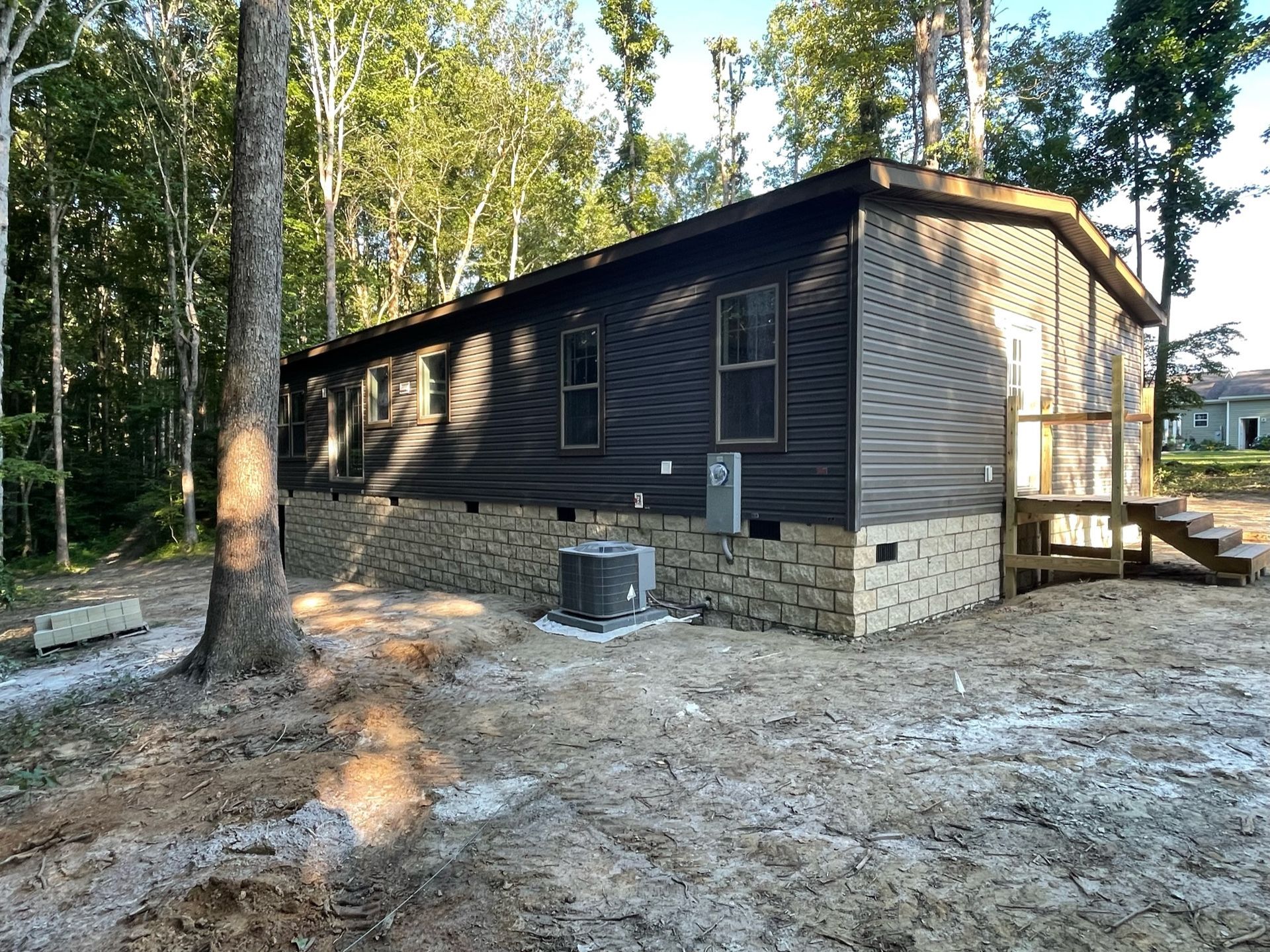A dark-sided house with stone facade, steps, and air conditioner unit in a wooded area.