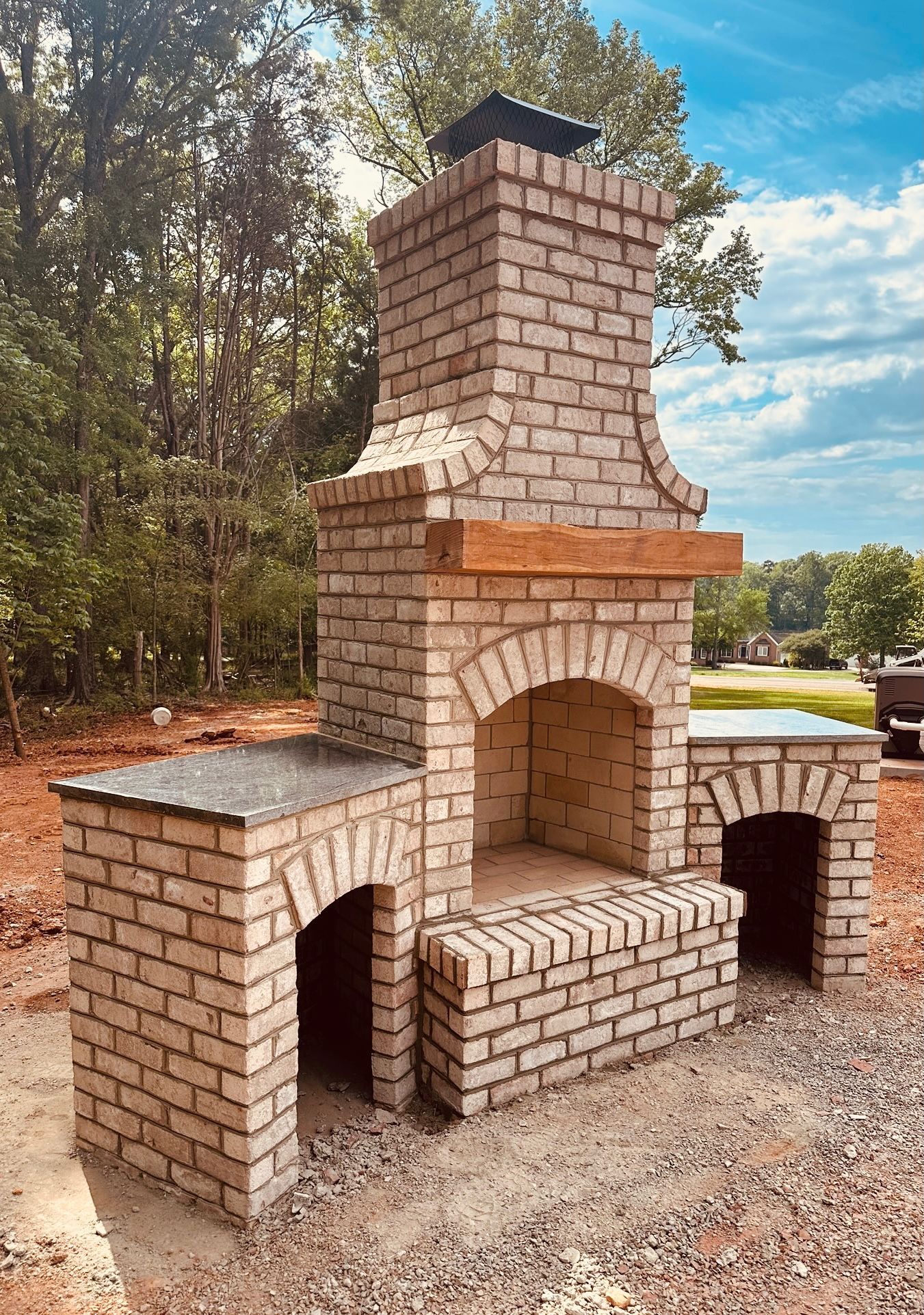 Brick outdoor kitchen with chimney, fireplace, and counters, beige bricks, blue sky.