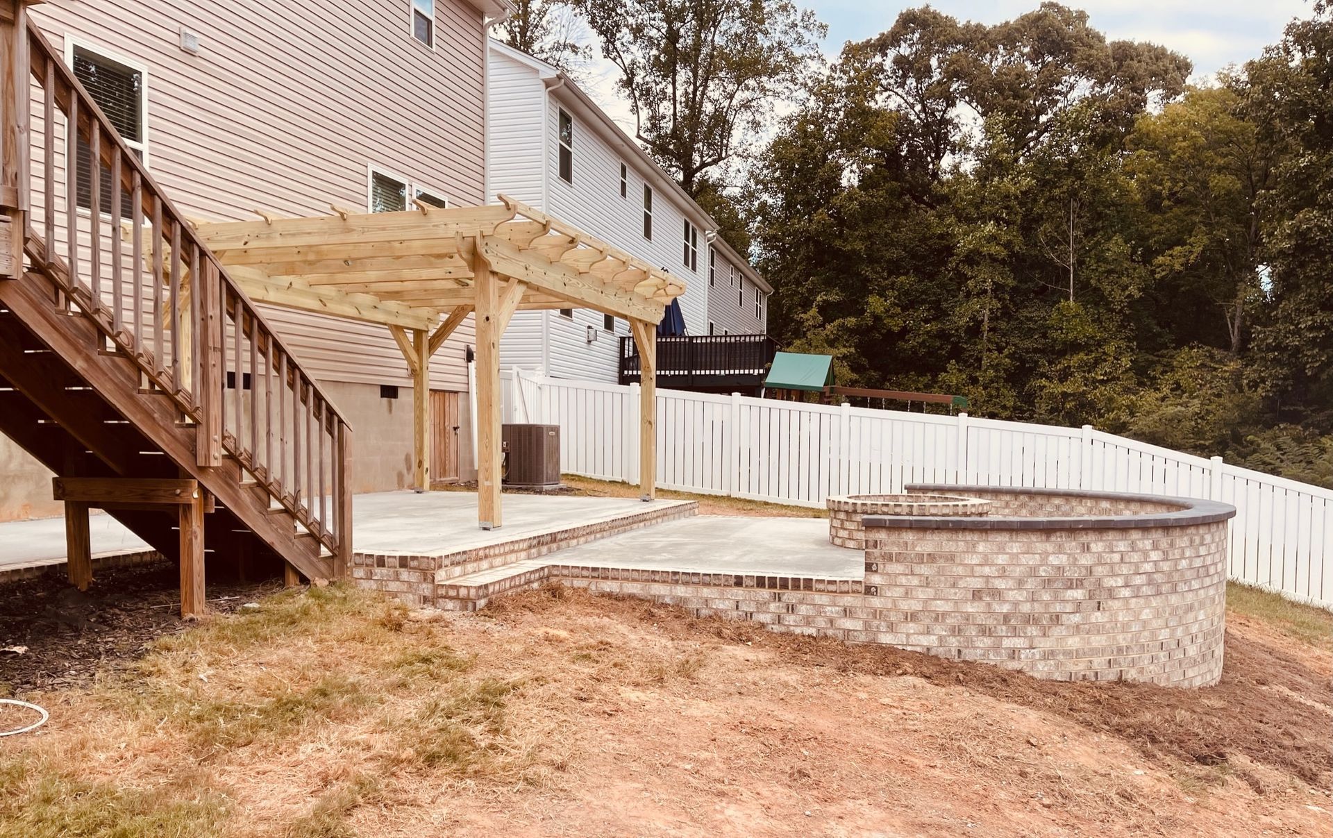 Backyard patio with a pergola, brick seating area, wooden deck, and white fence.