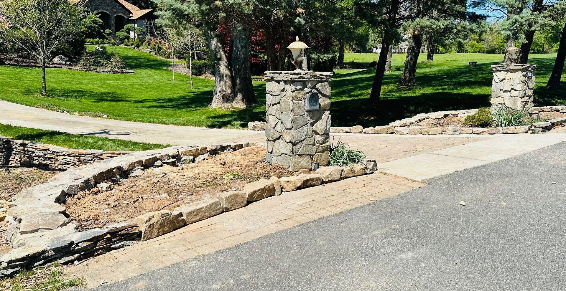 Stone entrance pillars with a gravel walkway and grass.