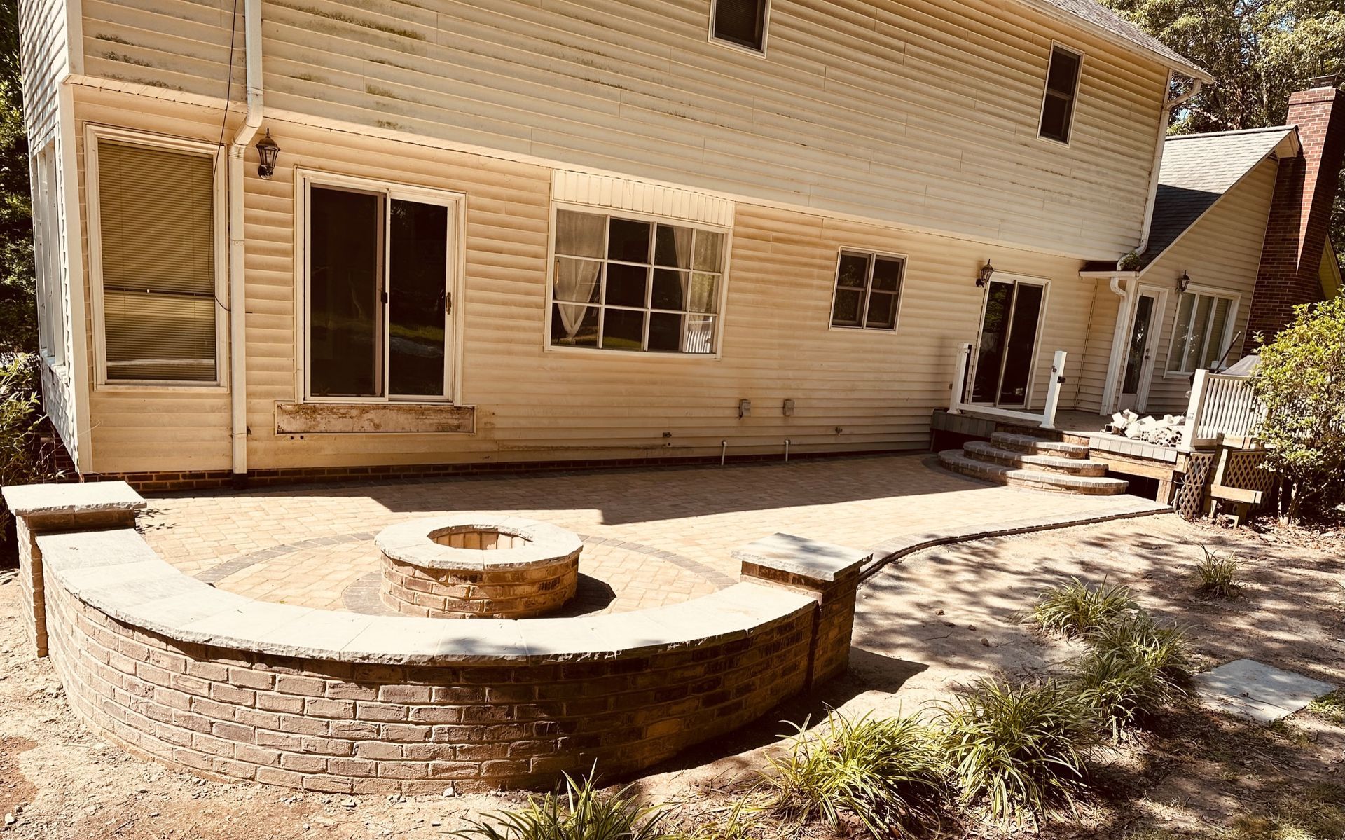 A backyard with a brick fire pit, patio, and light-colored house with sliding doors.