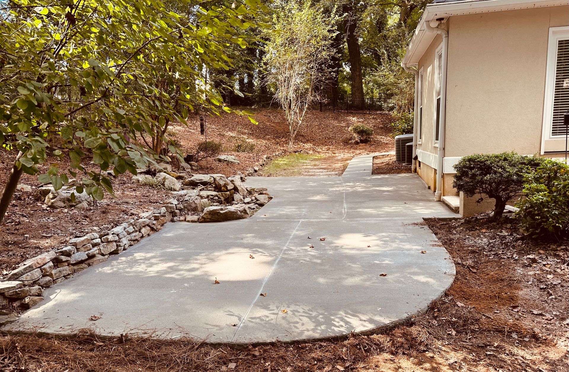 Concrete patio next to a beige house, surrounded by trees and dry brush.