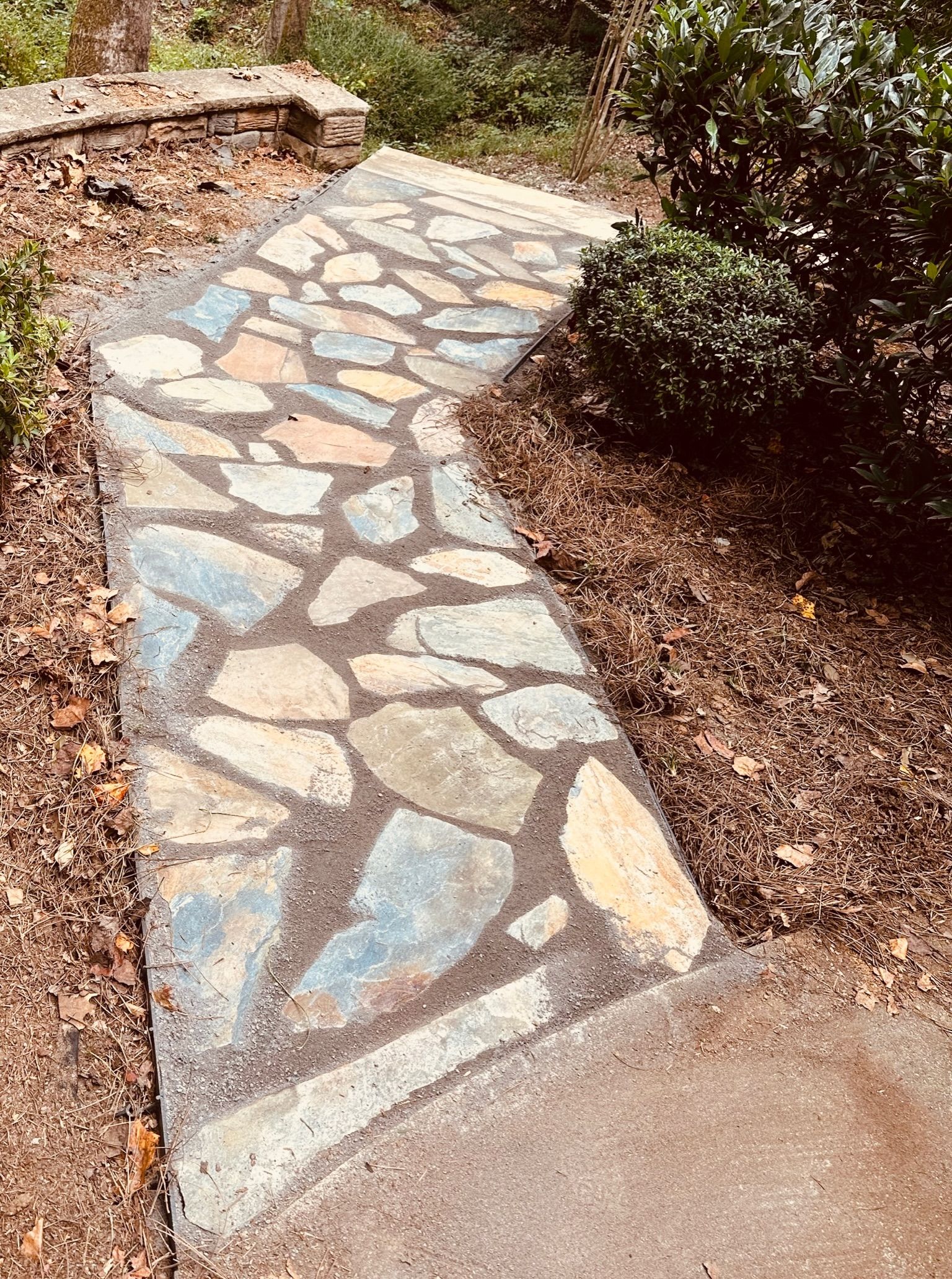 Stone pathway winding through a garden, with irregular, colorful stones and dark grout.
